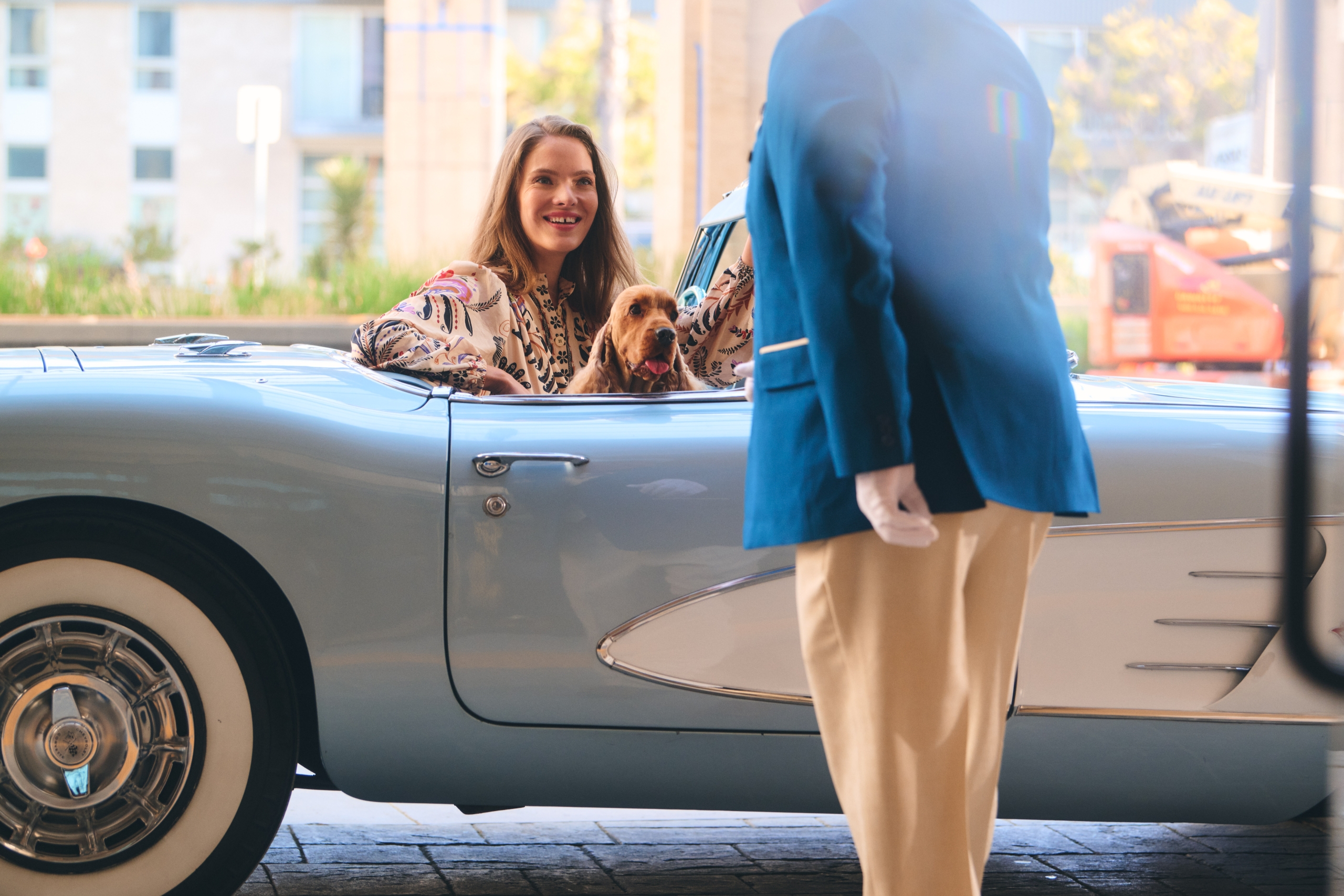 woman sitting in blue car with puppy smiling at bellman