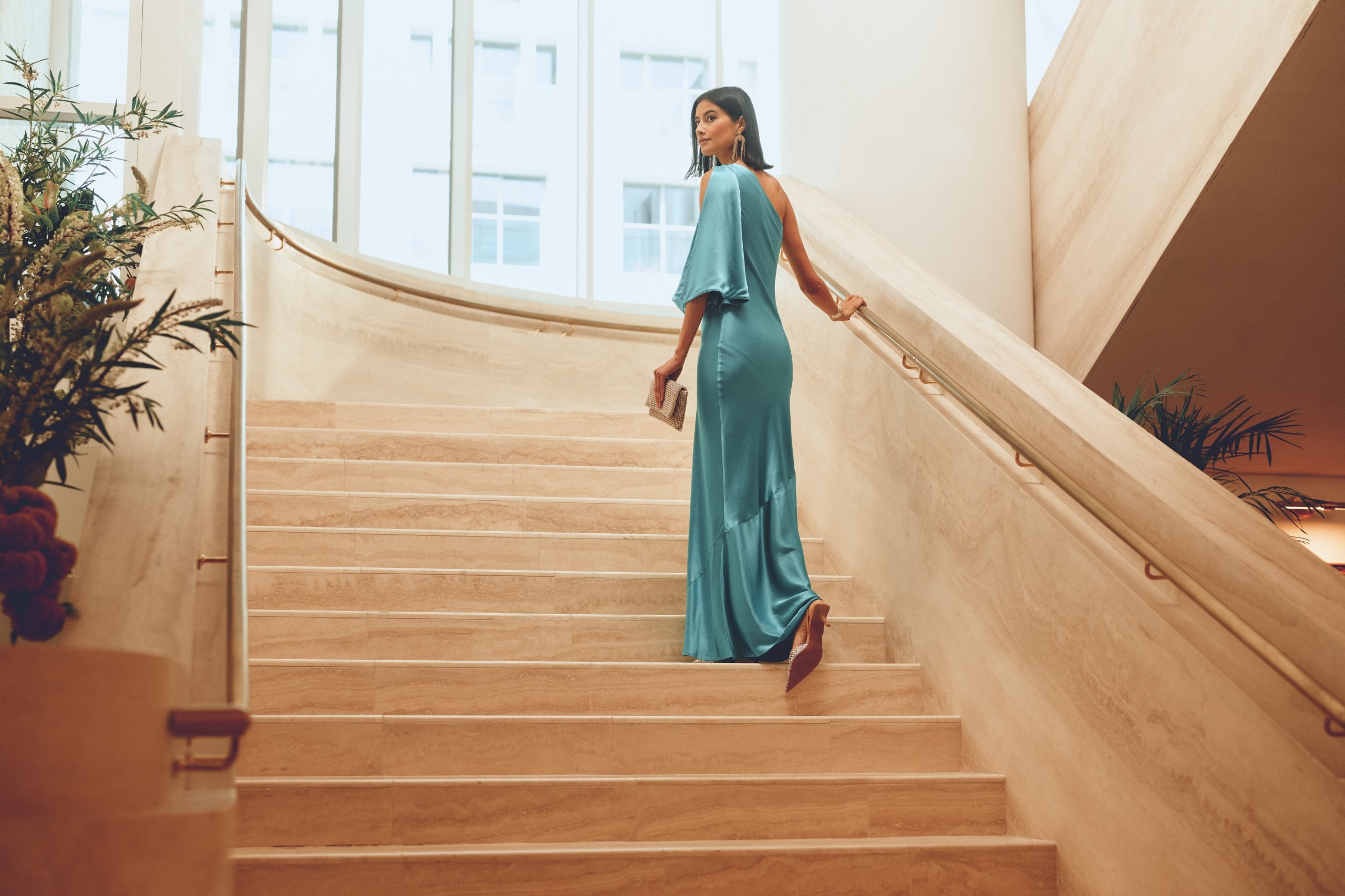 woman in long blue dress walking up stairs looking back