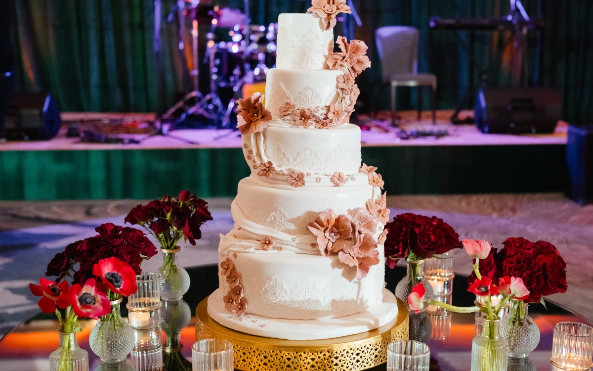 A high-angle, wide shot of a luxury wedding cake and event space at dusk. The scene features elegant lounge seating with d vibrant floral arrangements.