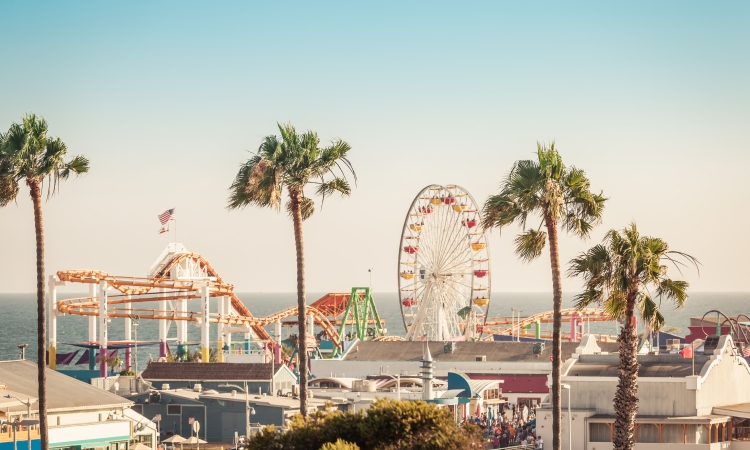 Famous amusement park with ferris wheeil in Santa Monica Los Angeles California in pastel ligt of sunset. Focus on palms