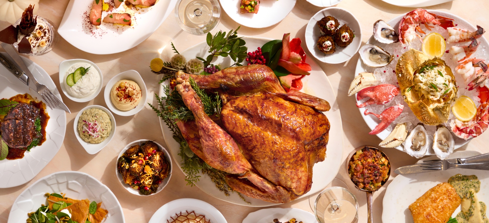 A golden-brown roasted turkey anchors a lavish spread of various gourmet dishes, including seafood, meats, salads, and side items, on a bright dining table.